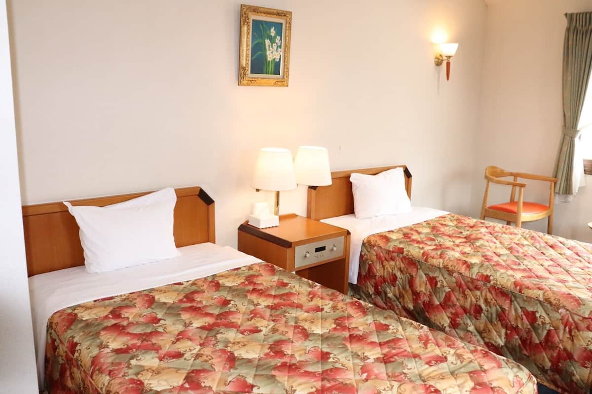 A hotel room with two beds, a nightstand with lamps, a chair, and a wall-mounted picture.