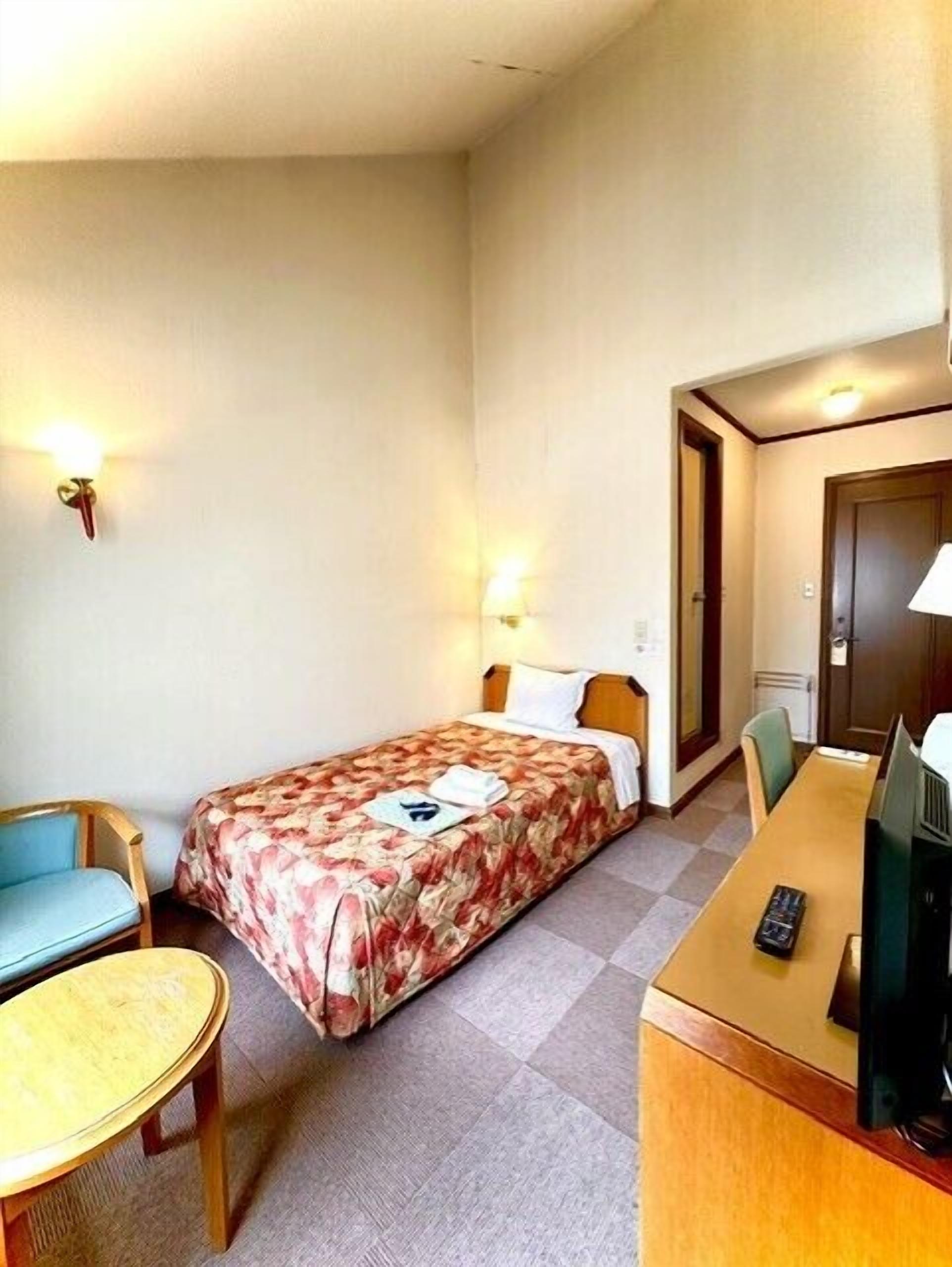 Habitación de hotel con una cama individual, un escritorio con computadora, una silla y una mesita.