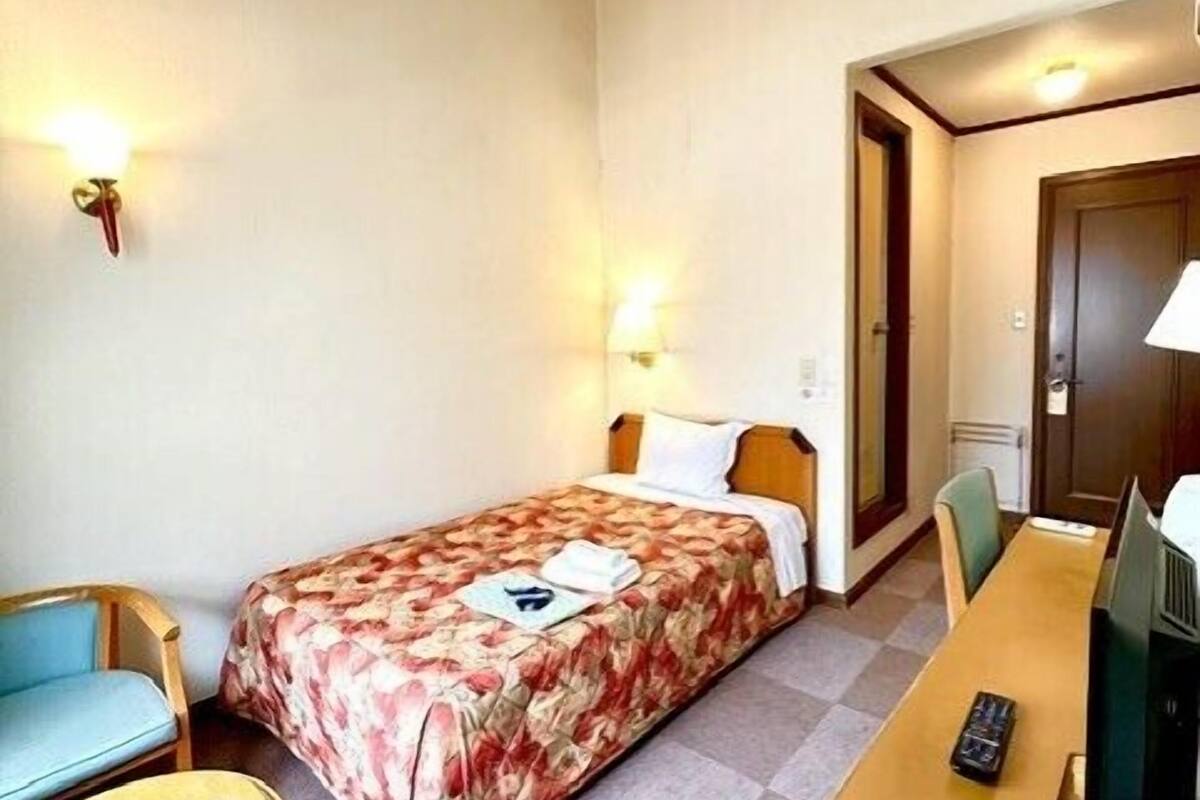 A hotel room with a single bed, a desk with a computer, a chair, and a small table.