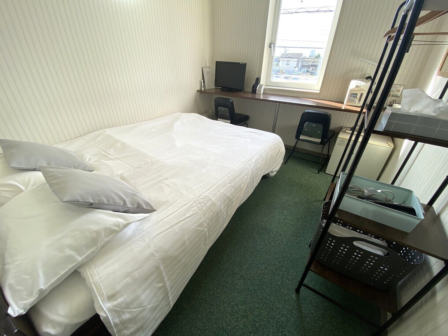 Een enkel bed met kussens, een bureau met een computer, een stoel, een stapelbed en een raam met uitzicht.