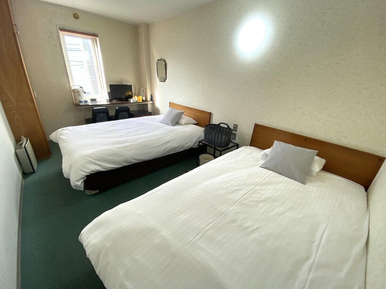 Een hotelkamer met twee bedden, een bureau met stoelen, een raam en een spiegel.