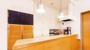 A kitchen with wooden cabinets, a countertop, a coffee maker, and pendant lights. - Hotel Goro Hakodate (Hakodate)