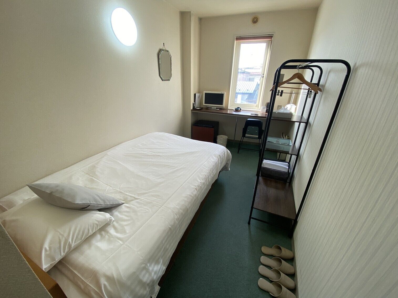 Een enkel bed met kussen, een bureau met computer, een stoel en een radiator.
