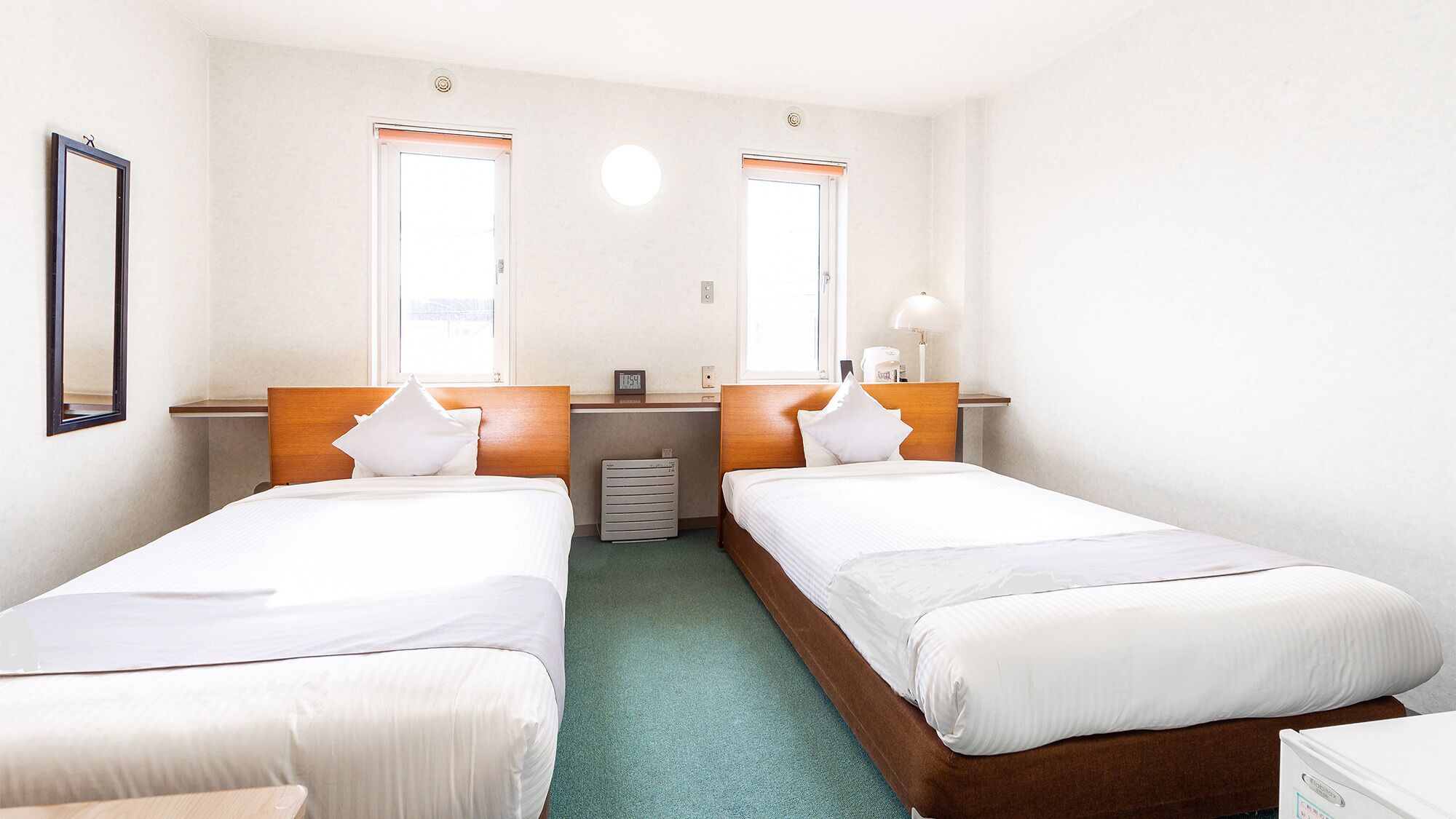 Een hotelkamer met twee bedden, een bureau, een stoel, een verwarming en een raam.
