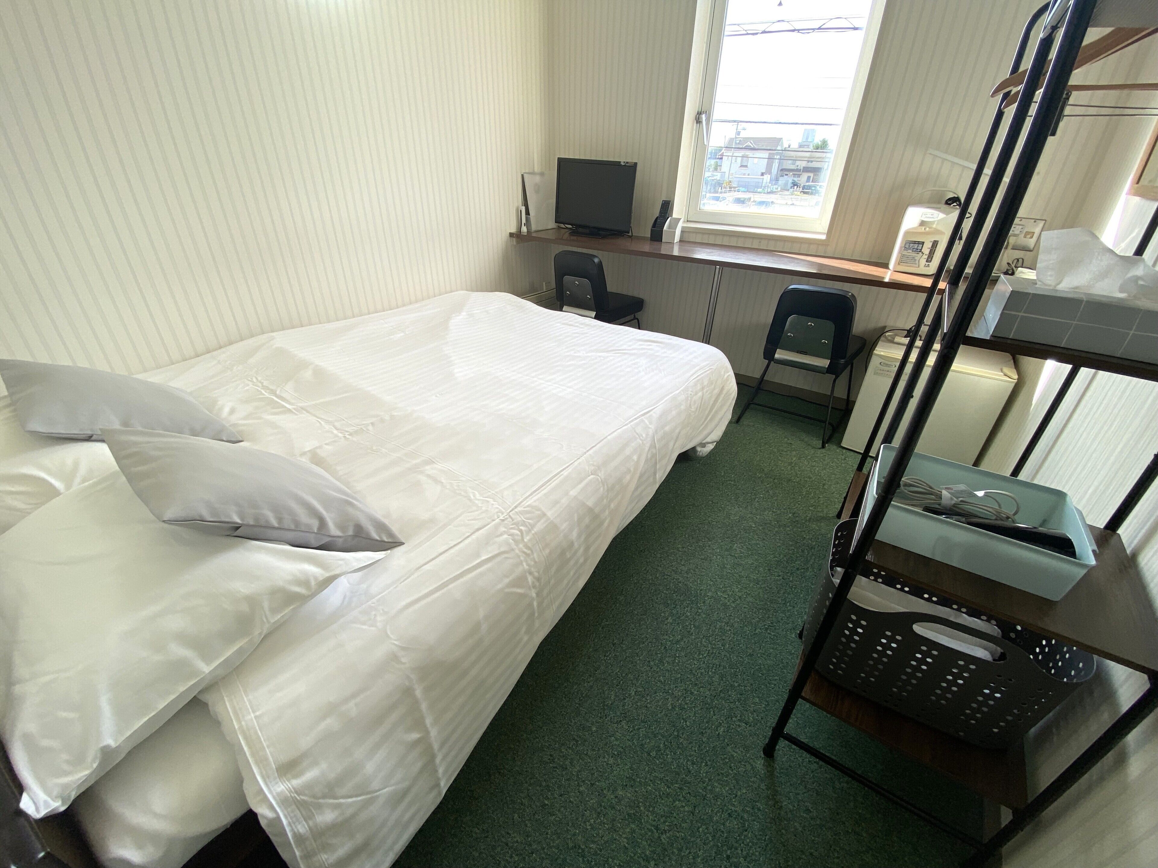 Een enkel bed met kussens, een bureau met een computer, een stoel, een stapelbed en een raam met uitzicht.