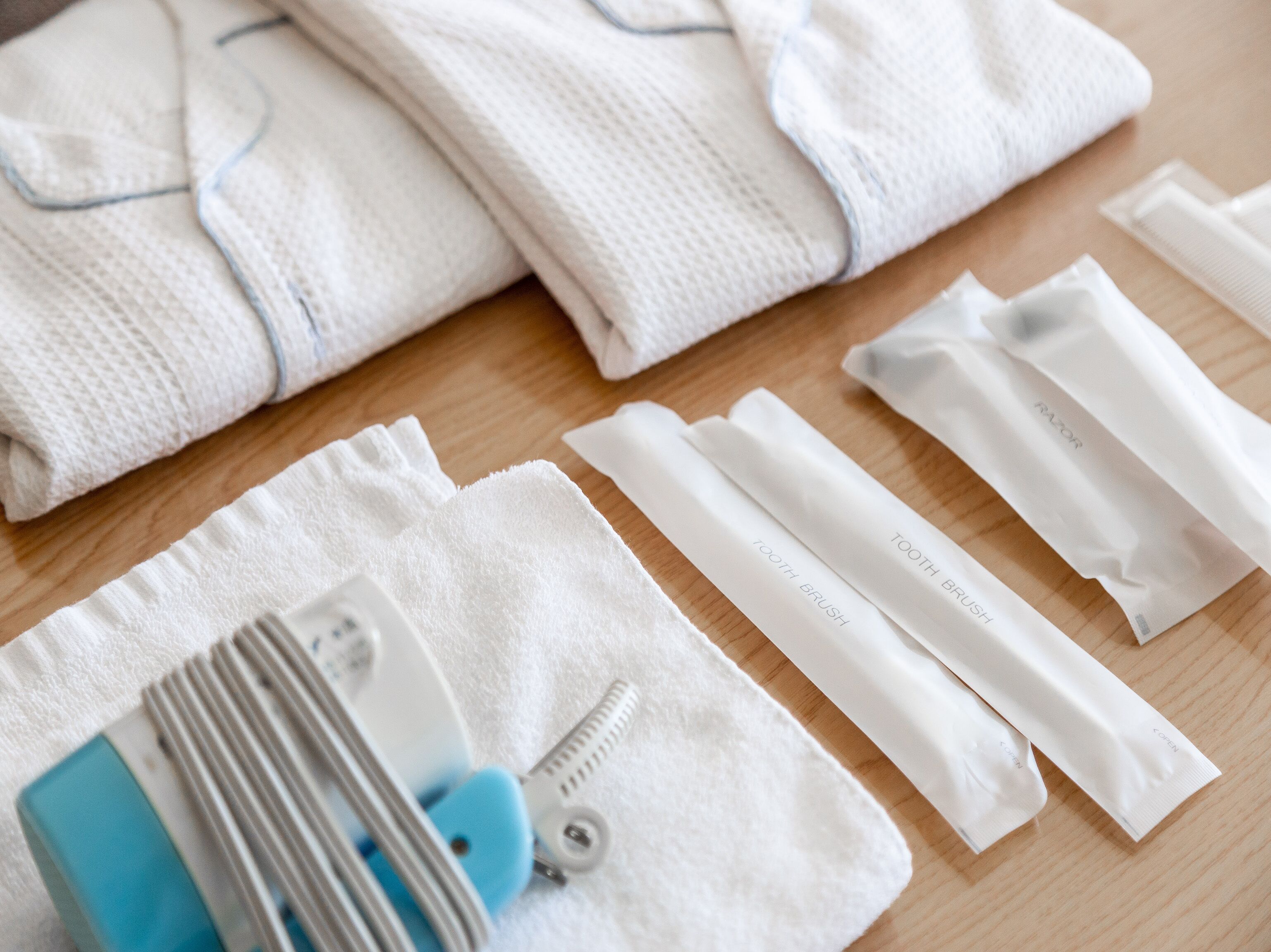 A neatly arranged set of white towels, a blue and white toothbrush, and a white dental floss package on a wooden surface.