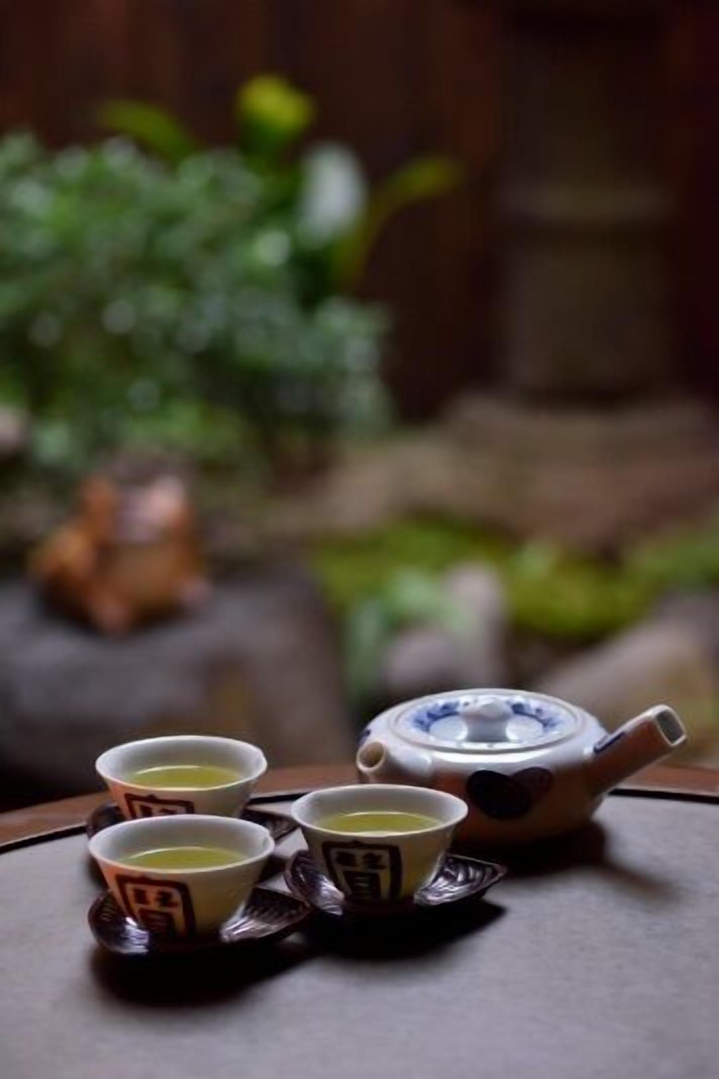 A teapot and four cups on a table with a blurred background.