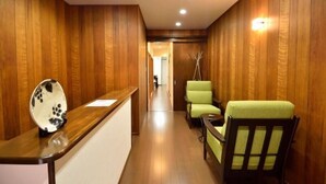 Un espace d’accueil avec un comptoir de réception en bois, un fauteuil vert et un mur en bois.