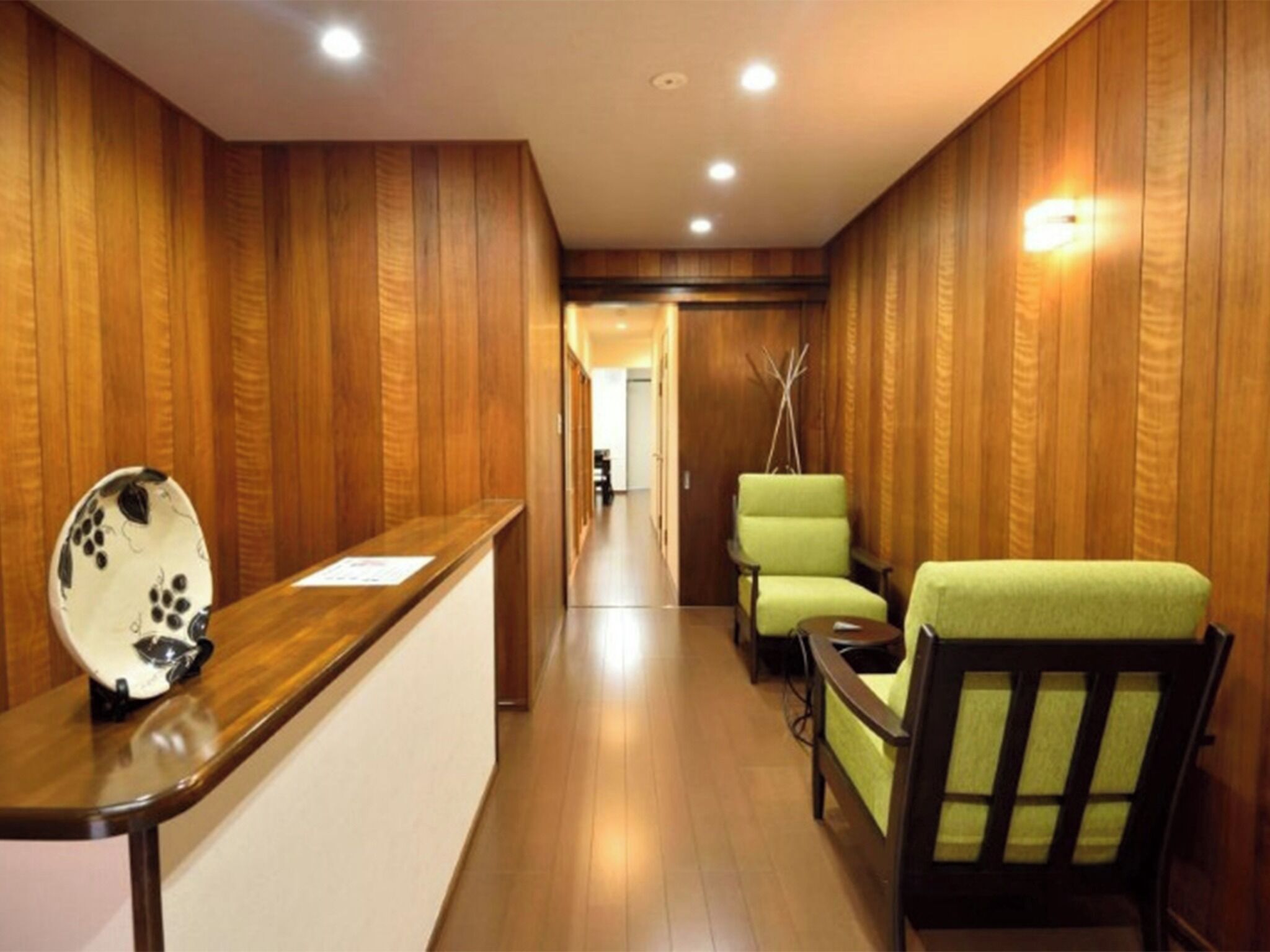 A reception area with a wooden reception desk, two green chairs, and a wooden wall with vertical panels.