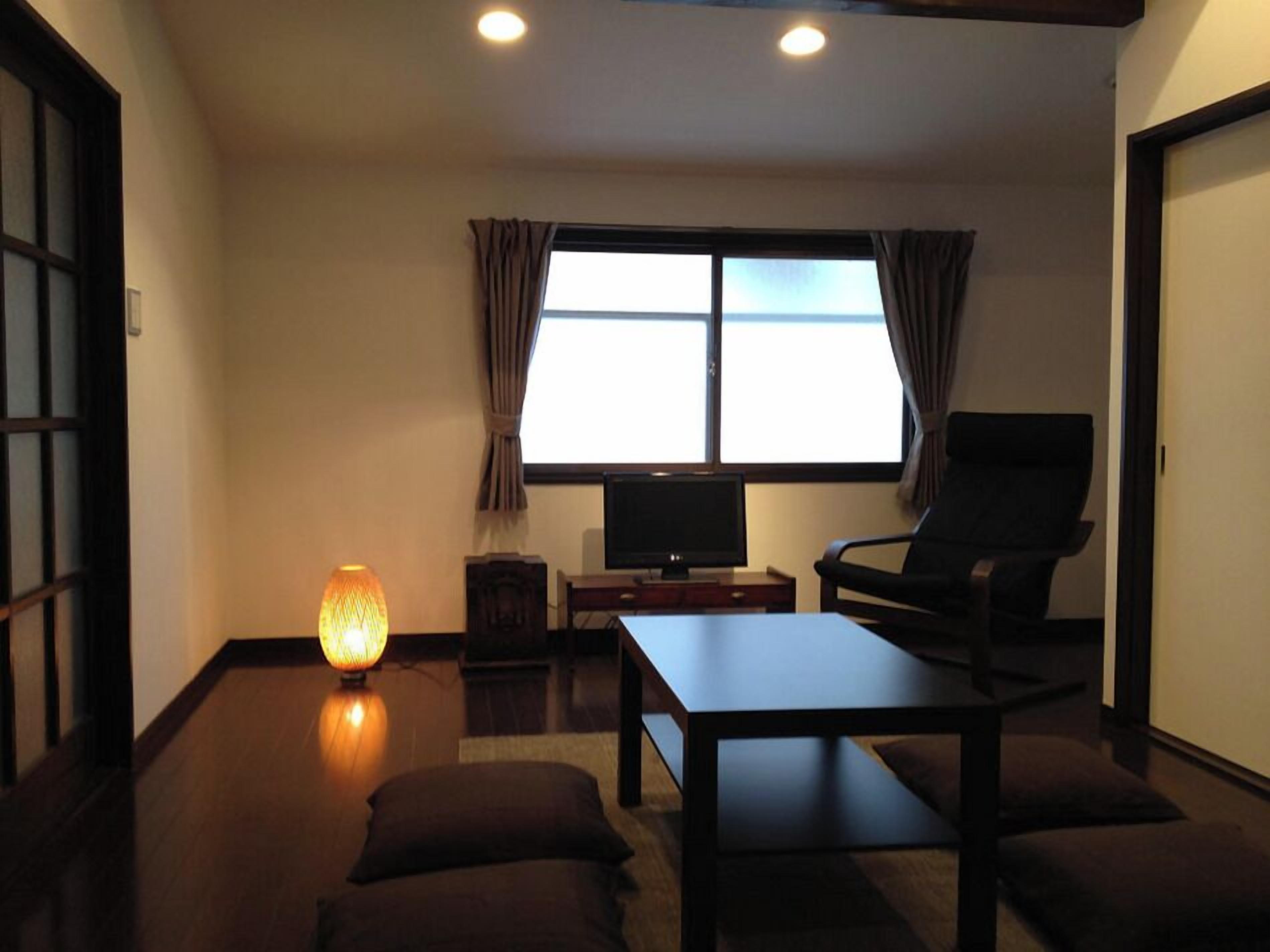 A room with a bed, a TV, a chair, a table, and a window with curtains.