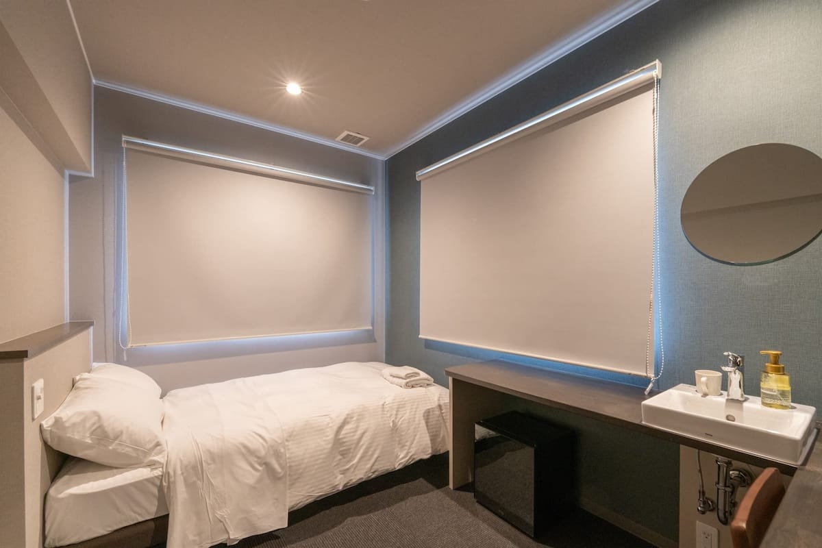 A hotel room with a bed, a desk with a sink, and a mirror.