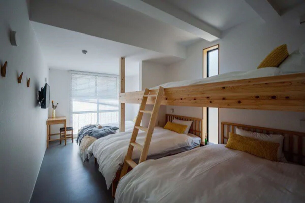 A bunk bed room with a ladder, a desk, and a window.