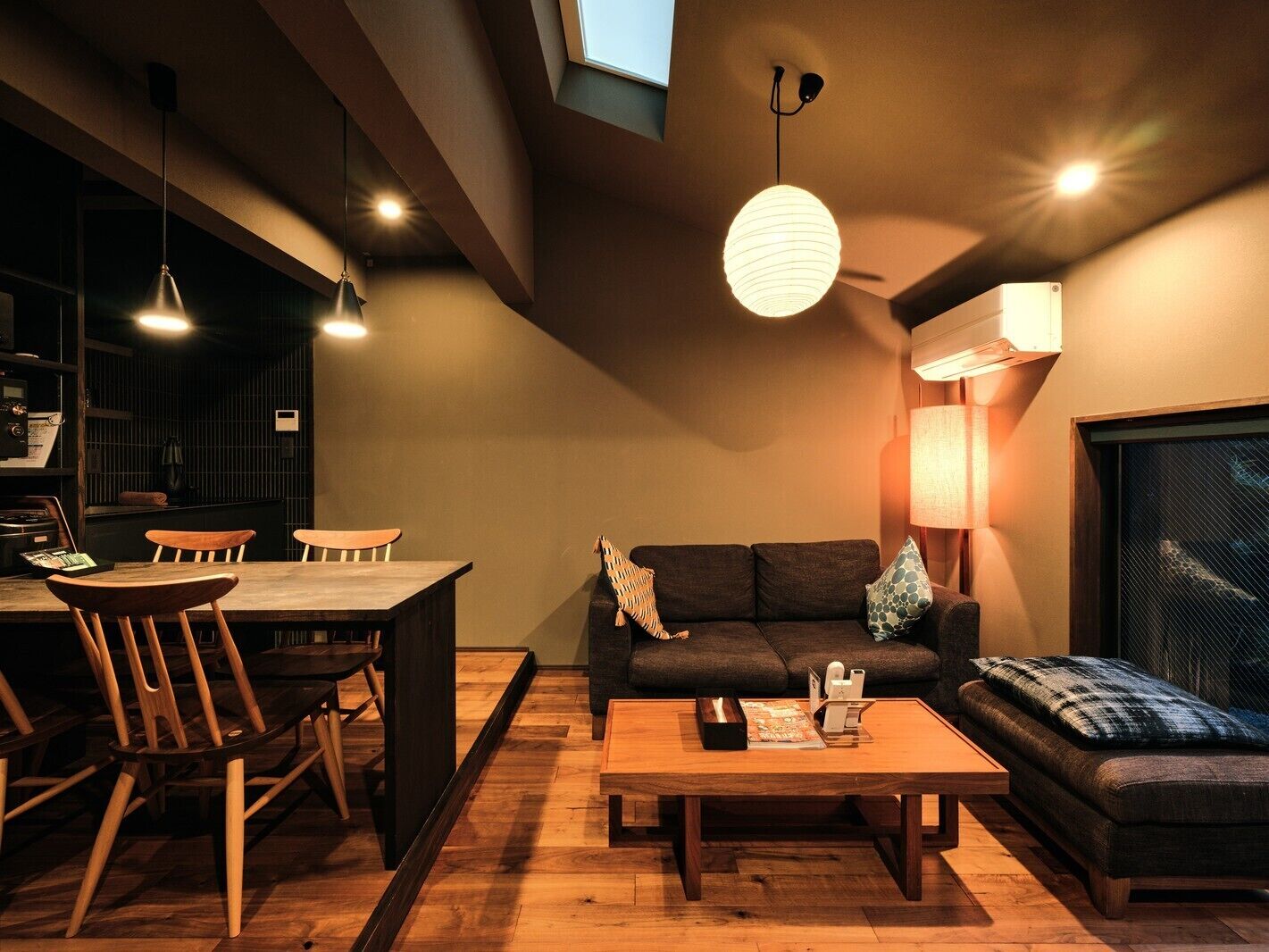 A modern living room with a dining area, wooden furniture, and a large window.