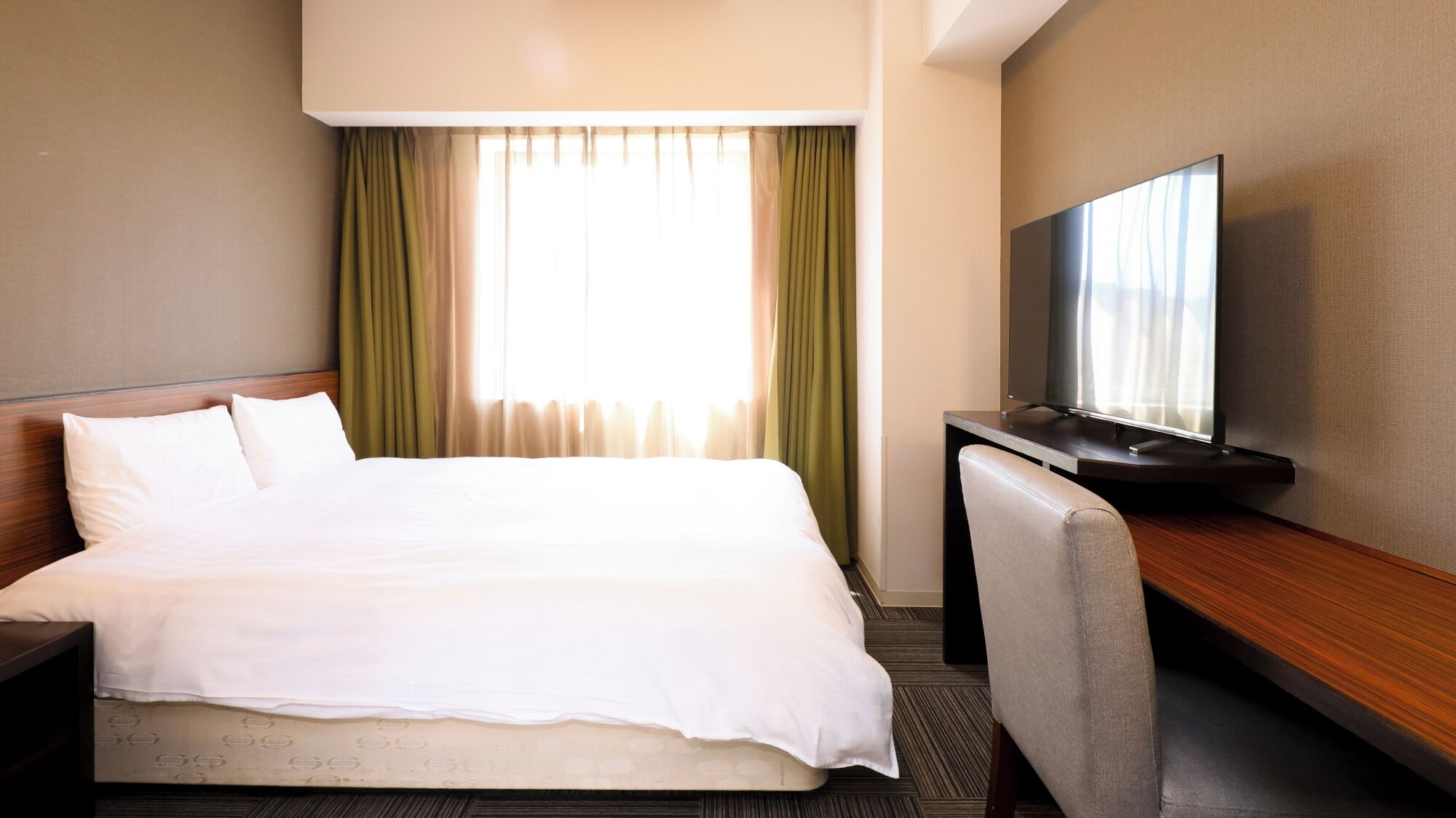 A hotel room with a bed, a desk with a television, and curtains.
