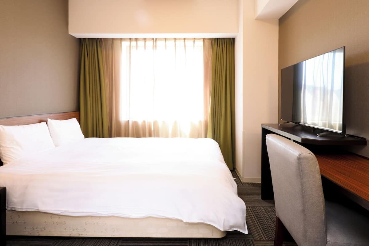 A hotel room with a bed, a desk with a television, and curtains.