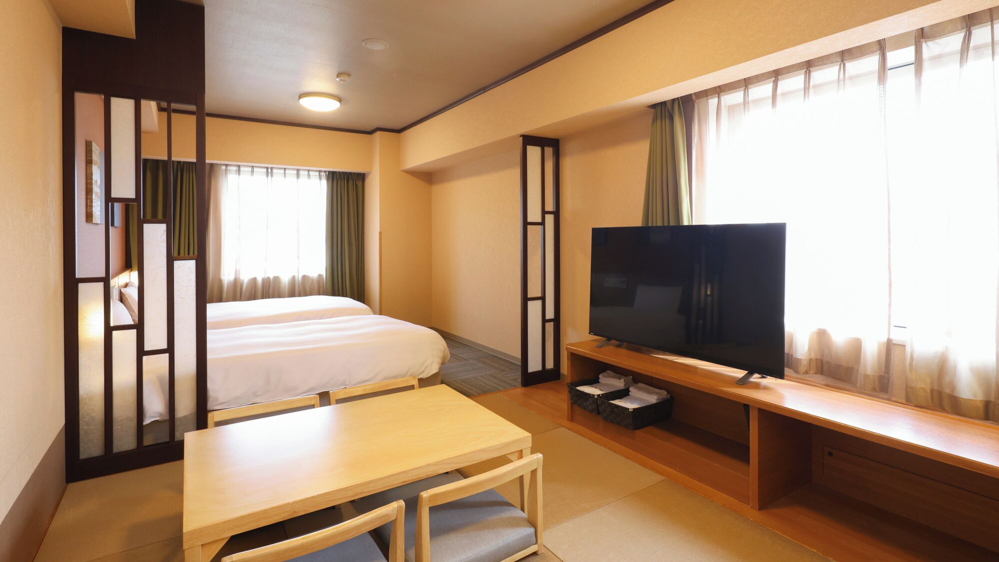 A hotel room with a bed, a TV, a desk, and a window with curtains.