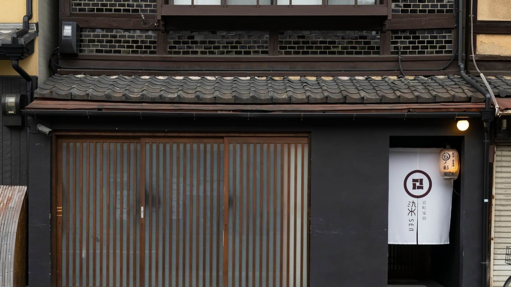 A traditional Japanese building with a large wooden door, a tiled roof, and a sign with Japanese characters.