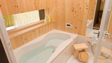 A wooden-paneled bathroom with a bathtub, a small wooden stool, and a shower area.
