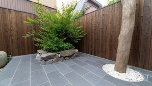 A paved patio area with a wooden fence, a tree, and a rock feature. - SEN Toji Uomitsu (Kyoto)