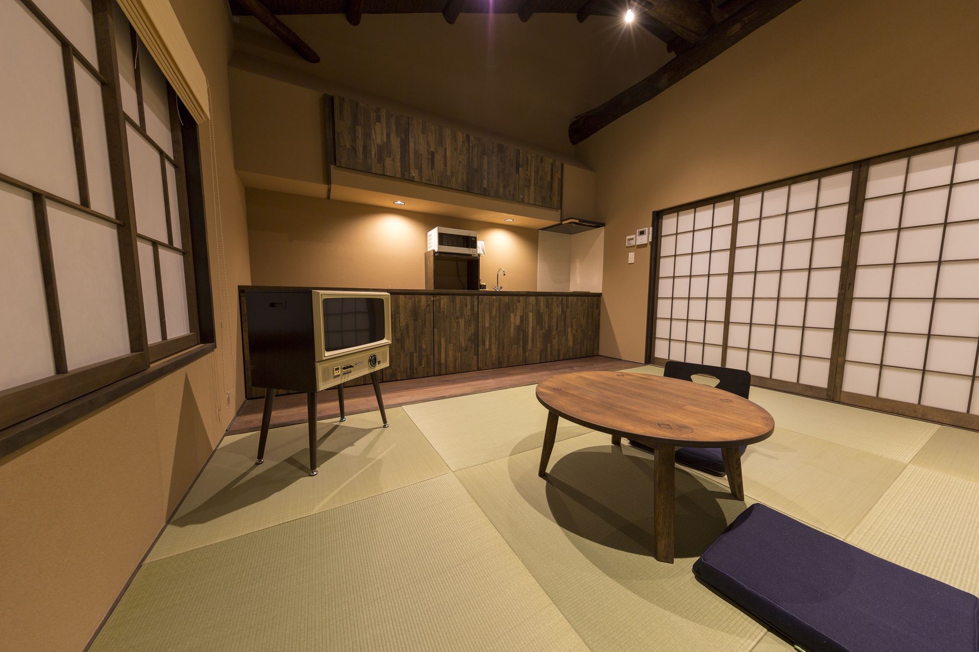 A traditional Japanese-style room with tatami flooring, a low table, and a television on a stand.