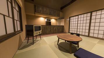 A traditional Japanese-style room with tatami flooring, a low table, and a television on a stand.