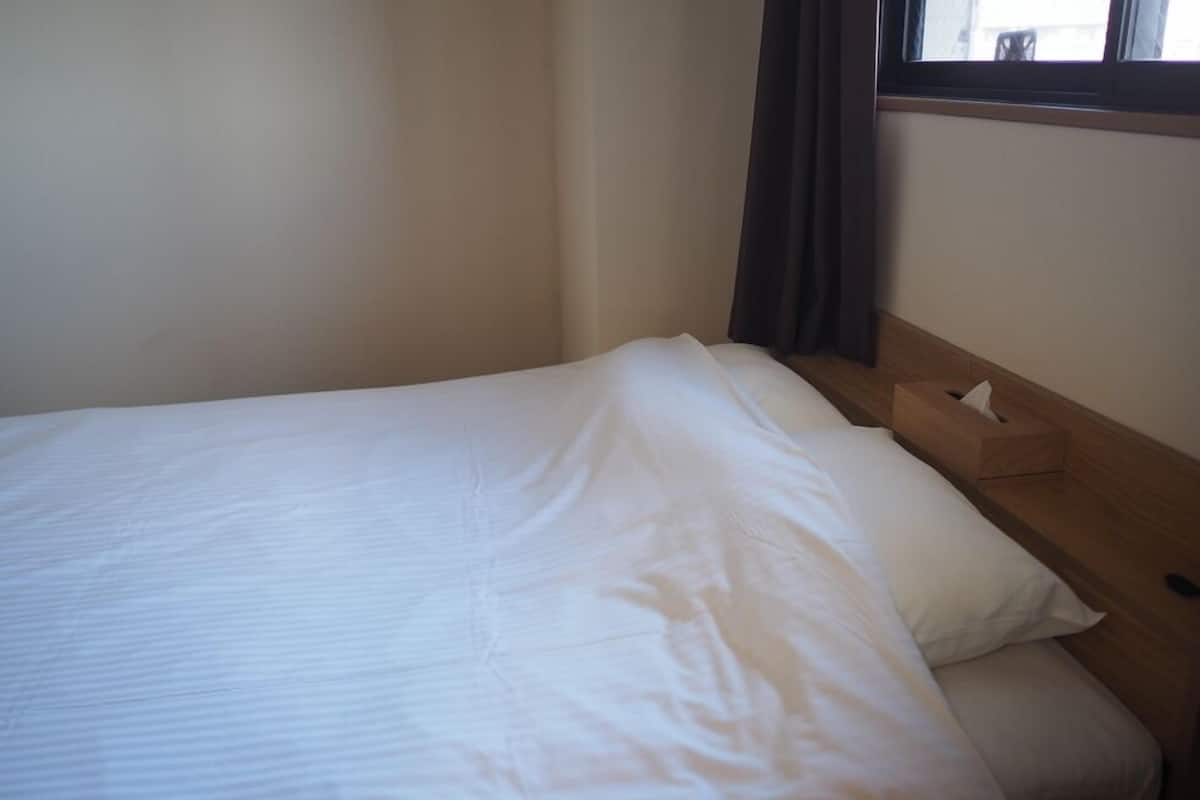 Un lit simple avec une literie blanche, une tête de lit en bois et une table de chevet sur laquelle se trouve une boîte de mouchoirs.