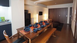 A dining area with a long wooden table set for six, a kitchen with a microwave and refrigerator, and a dark wooden door. - Asakusa Eight (Tokyo)
