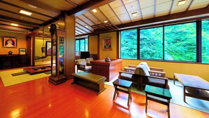 A traditional Japanese-style room with tatami flooring, a low wooden desk, and a large window offering a view of greenery.
