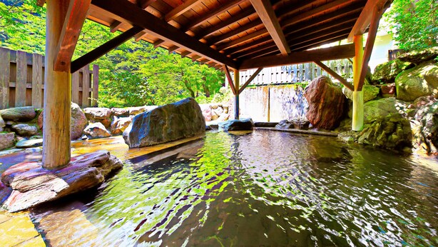 A wooden pavilion over a water feature with rocks and greenery.