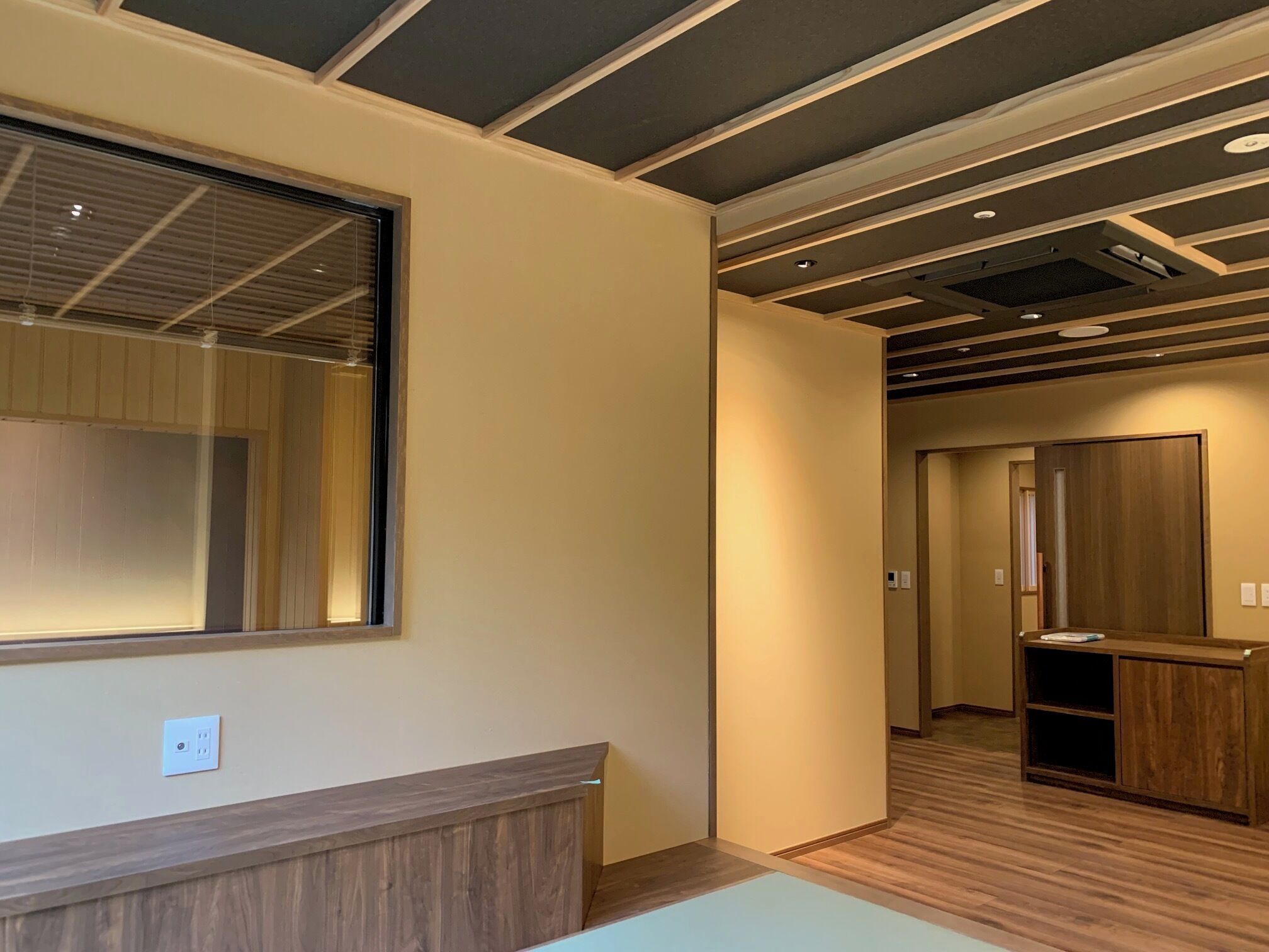 A hotel room with a large window, wooden paneling, a reception desk, and a hallway leading to another room.