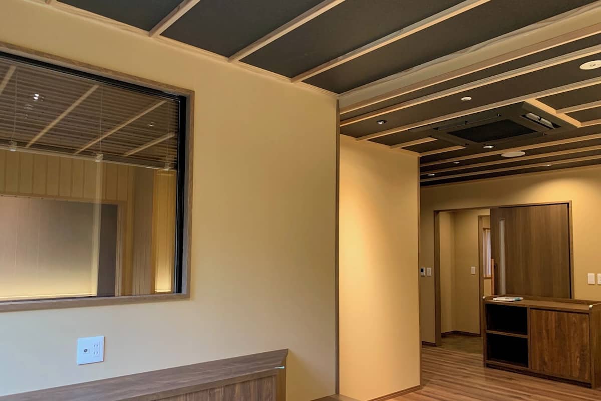A hotel room with a large window, wooden paneling, a reception desk, and a hallway leading to another room.
