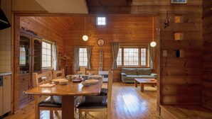 Interior de uma cabana de madeira com mesa de jantar, cadeiras, um sofá e uma cozinha.