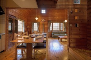 A wooden cabin interior with a dining table, chairs, a sofa, and a kitchen area. - Sapphire (Kutchan)