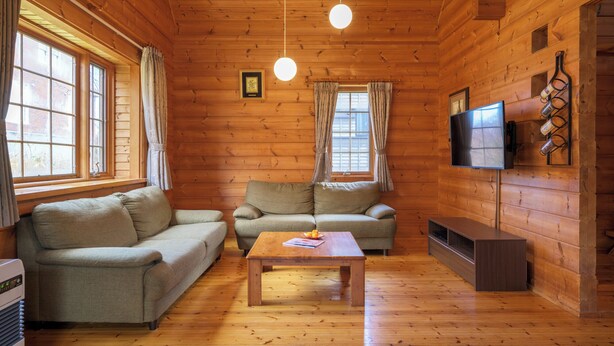 Interior de uma cabana de tronco com um sofá, uma mesa, uma televisão e uma lareira.