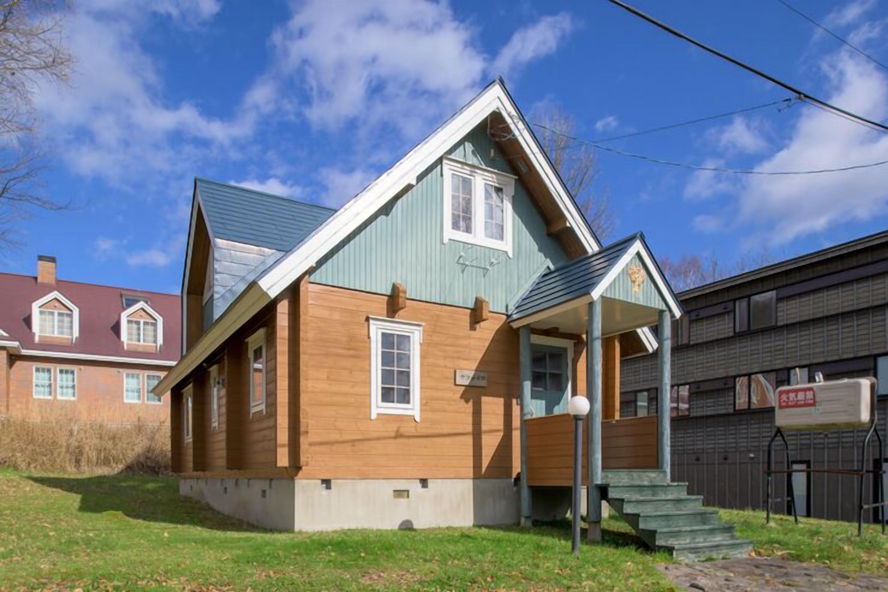 A two-story wooden house with a gabled roof, a front porch, and a visible mailbox.