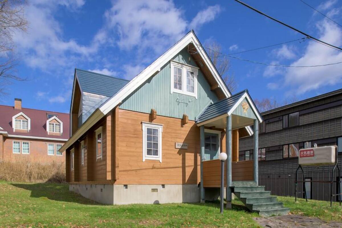 A two-story wooden house with a gabled roof, a front porch, and a visible mailbox.