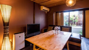 A room with a wooden table, a TV, a modern air conditioner, and a view of a garden through a sliding door. - Maiko-han Inn (Kyoto)