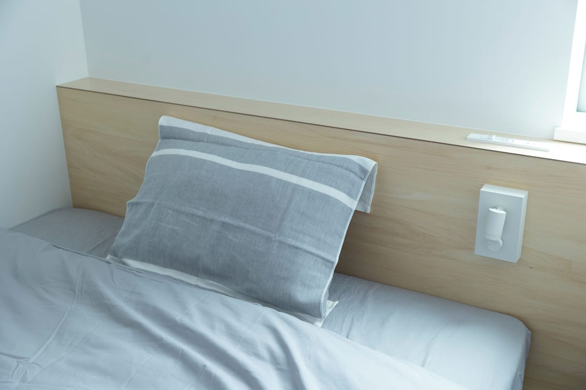 Ein Bett mit Kopfteil, einem Kopfkissen und einem wandmontierten Lichtschalter.