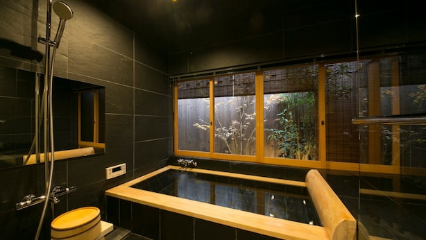 A modern bathroom with a large bathtub, a wooden bench, a shower, and a window with a view of trees. - Satoi Seishi Omiya Gojo (Kyoto)