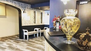 Een receptiezone met een marmeren vloer, een receptiebalie, een bank en een decoratieve vaas met bloemen.