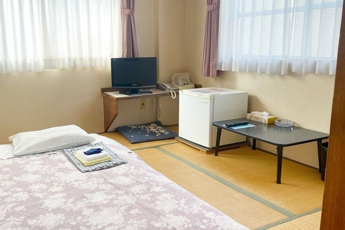 A hotel room with a bed, a desk with a computer, a refrigerator, and a small table.