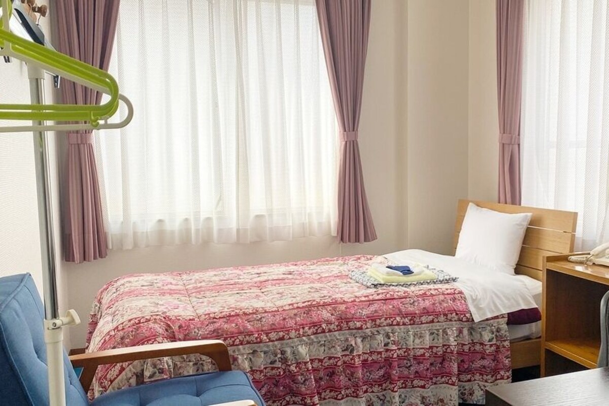 A hotel room with a bed, bedside table, chair, and a TV.
