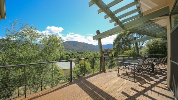 A wooden deck with a table and chairs, overlooking a mountainous landscape.
