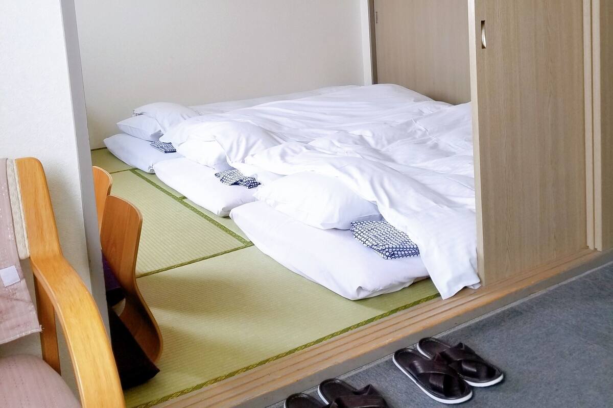 A single bed with white bedding, a wooden wardrobe, and a pair of slippers on the floor.