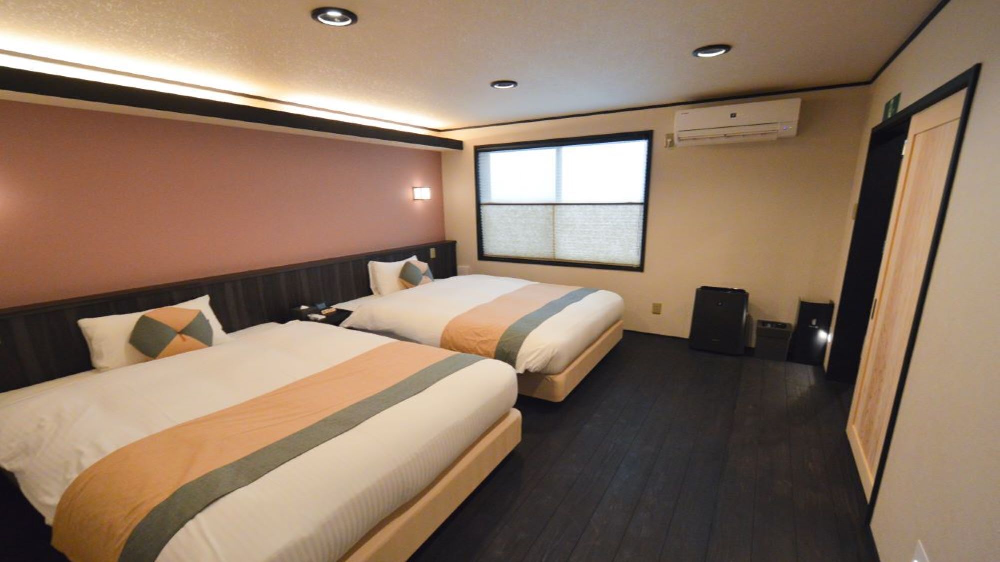 Ein Hotelzimmer mit zwei Betten, einem Fenster, einer Klimaanlage und einem Mülleimer.