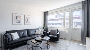 Een moderne woonkamer met een zwarte leren bank, twee fauteuils, een salontafel en een groot raam met uitzicht op gebouwen.