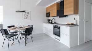 Een moderne keuken met witte kasten, een zwarte afzuigkap en een eethoek met een ronde tafel en stoelen.