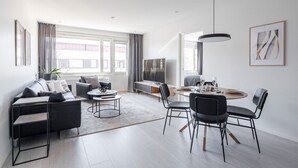 Een moderne woonkamer met een bank, salontafel, televisie, eettafel met stoelen en een groot raam met gordijnen.