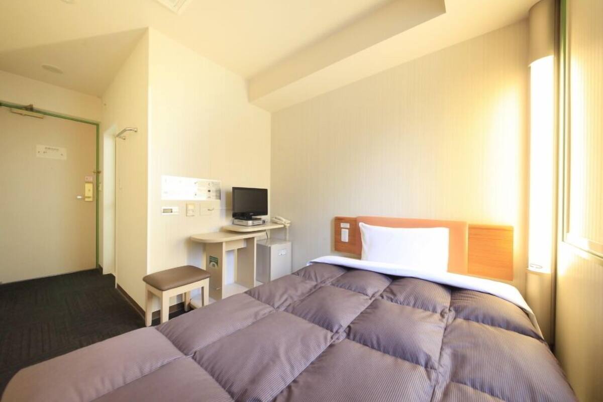 A hotel room with a bed, a desk with a computer, a chair, and a window.