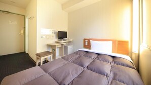 Quarto de hotel com uma cama, escrivaninha com computador, cadeira e uma pequena mesa.